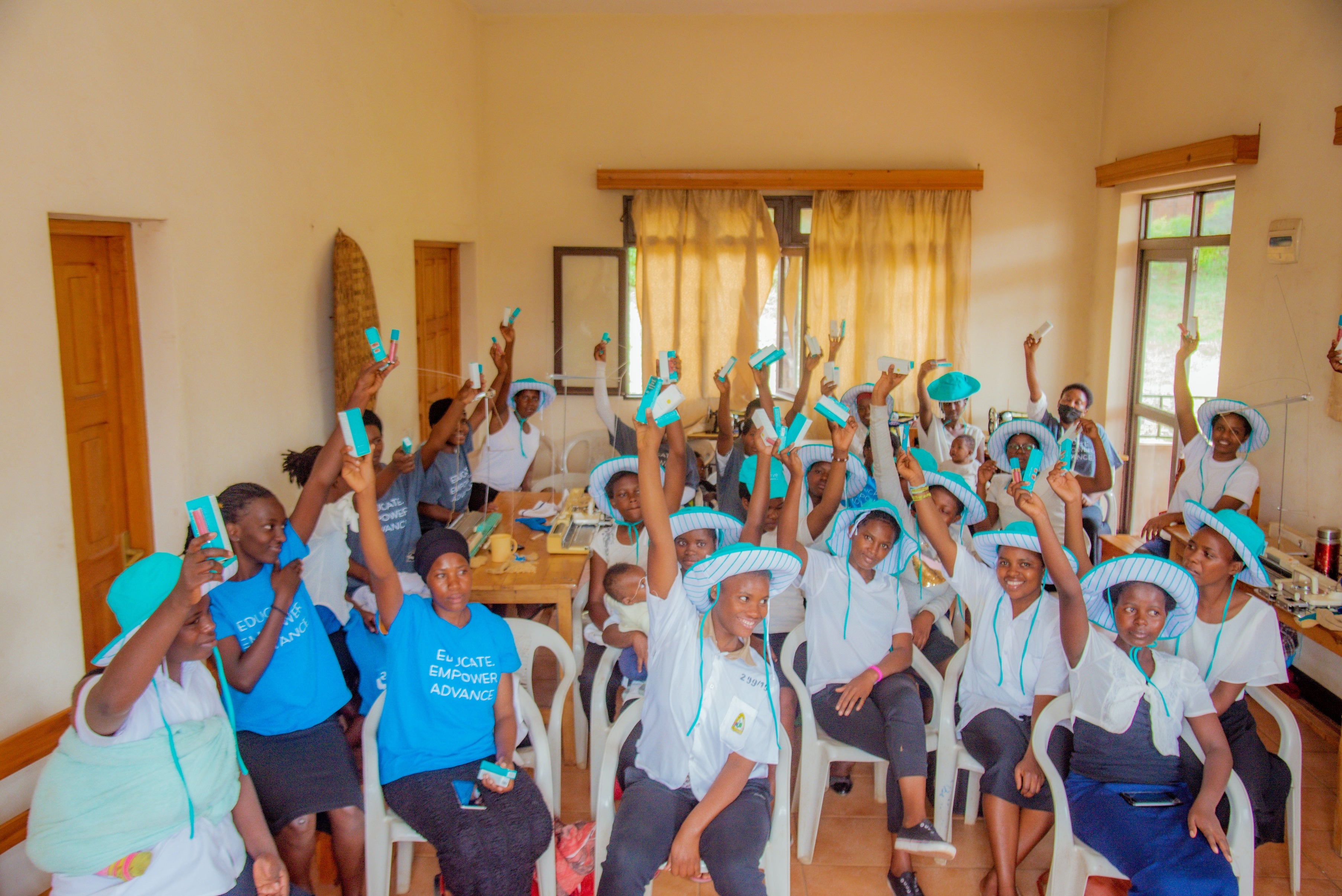 Group of people in matching hats and shirts holding up products with smiles in a classroom setting.