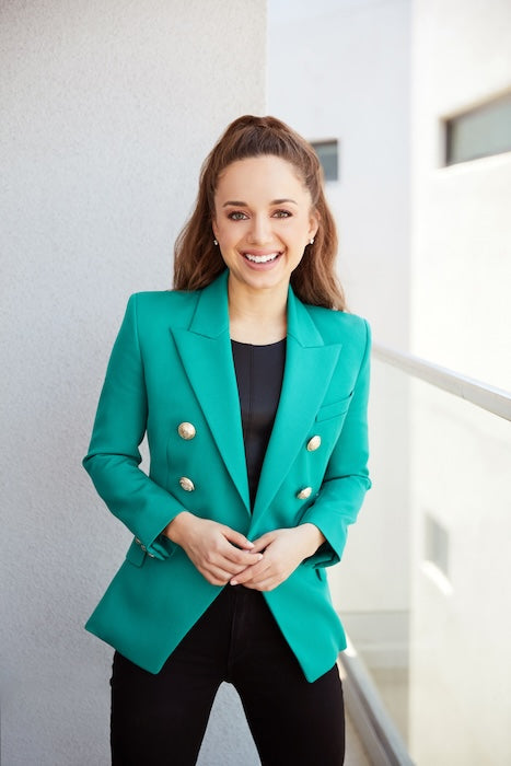 Smiling woman in a teal blazer standing on a balcony.
